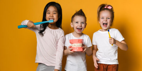 Three,Children,With,Toothbrushes,And,A,Dental,Implant,Model,Stand